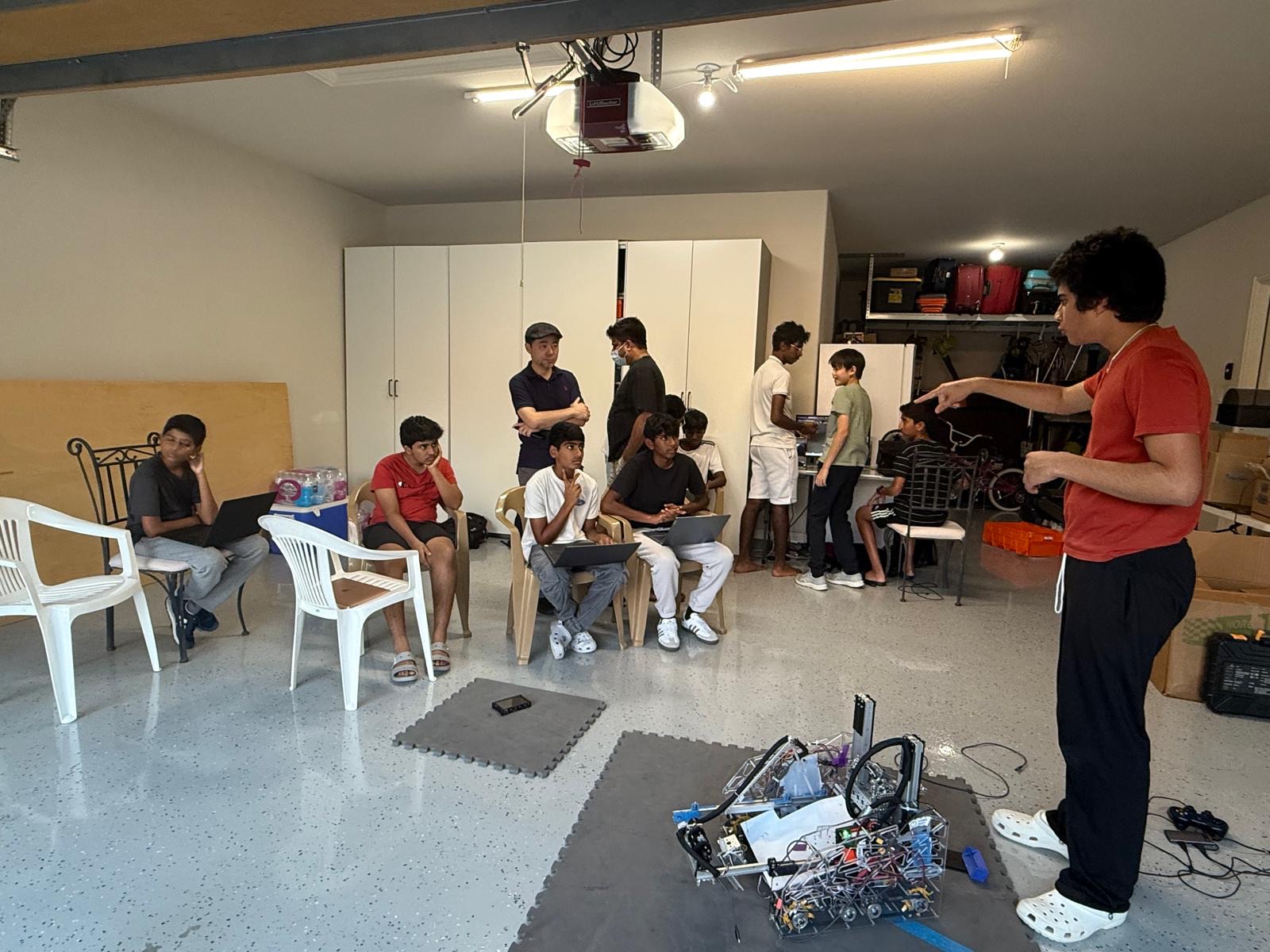 Team members gathered in a garage workshop for a meeting, with the robot on the floor in front of them