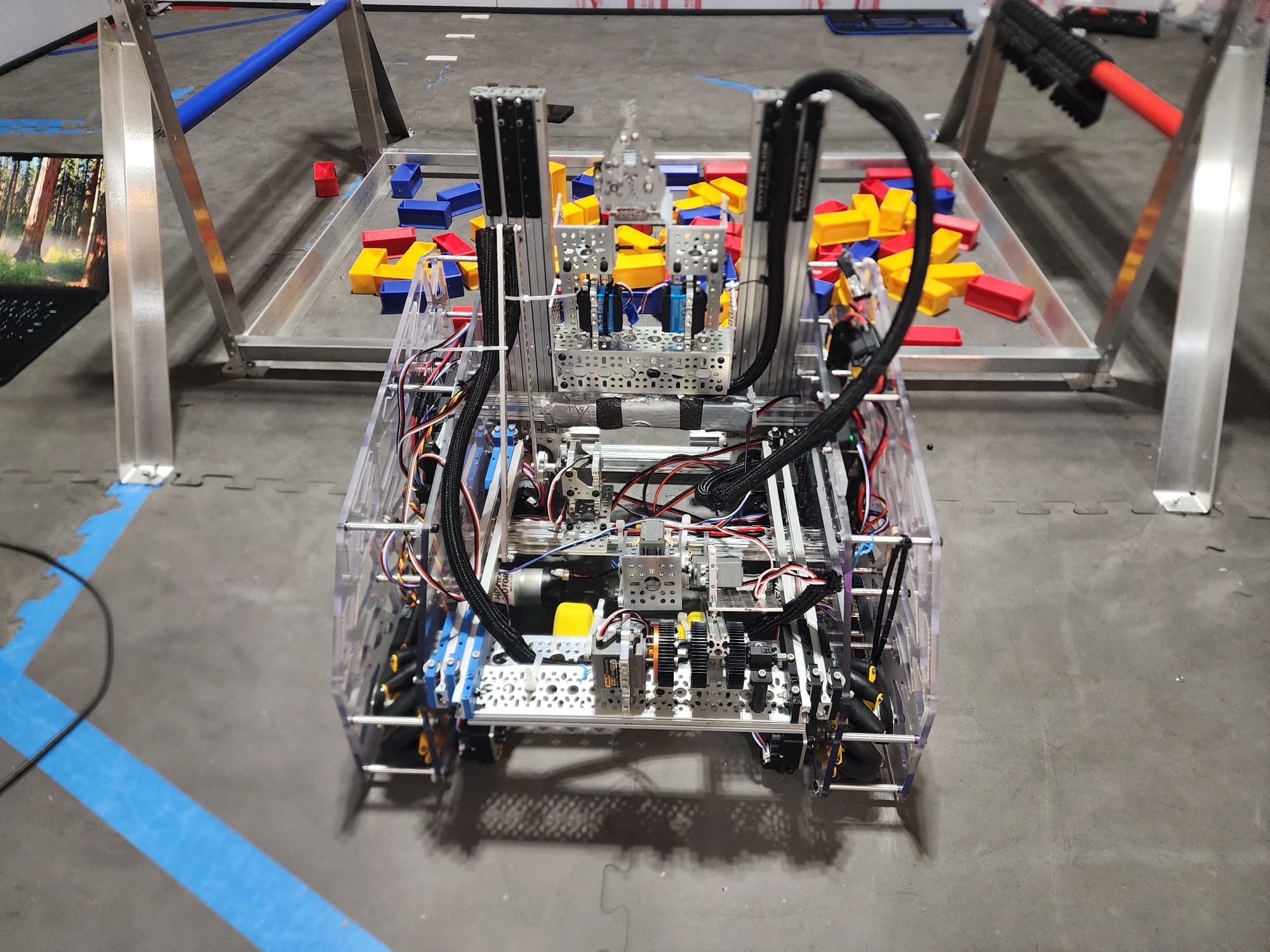 Nautilus, the 2024-25 robot, on the competition field beside a tray of yellow and blue game blocks